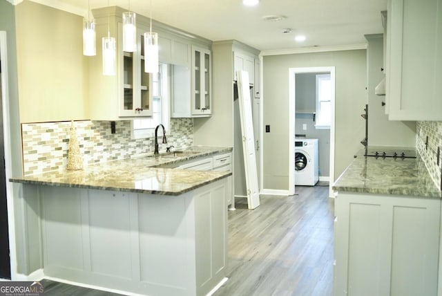 kitchen featuring a sink, washer / clothes dryer, a peninsula, glass insert cabinets, and light stone countertops