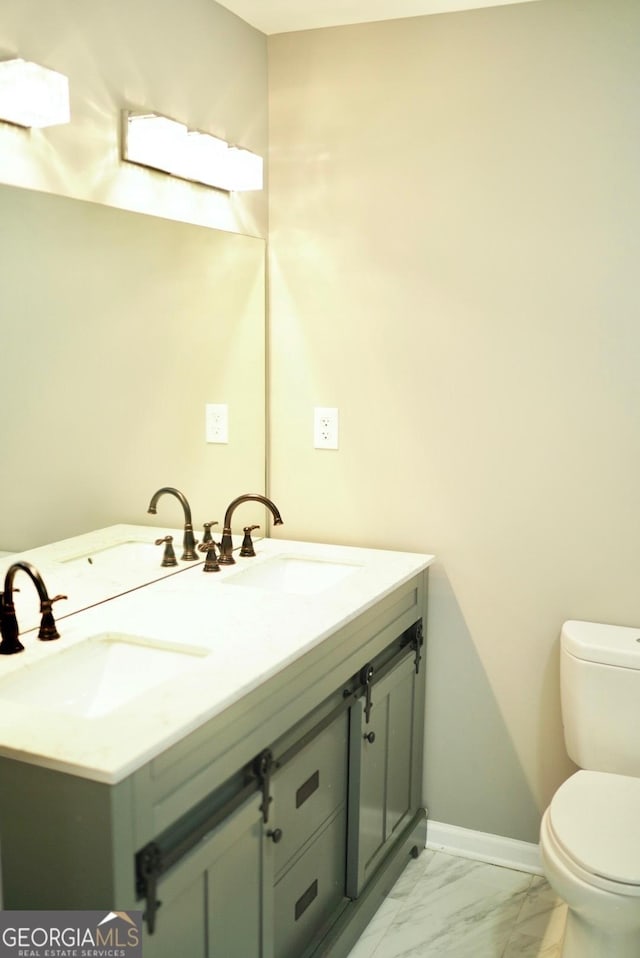 bathroom with double vanity, toilet, marble finish floor, and a sink