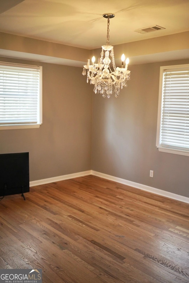 spare room with dark wood-type flooring, a notable chandelier, baseboards, and a wealth of natural light