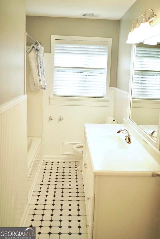 full bathroom with visible vents, a healthy amount of sunlight, vanity, and a wainscoted wall