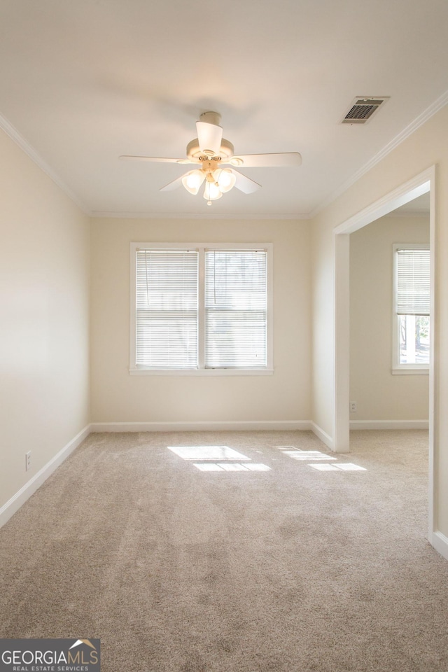 carpeted spare room featuring crown molding, baseboards, visible vents, and ceiling fan