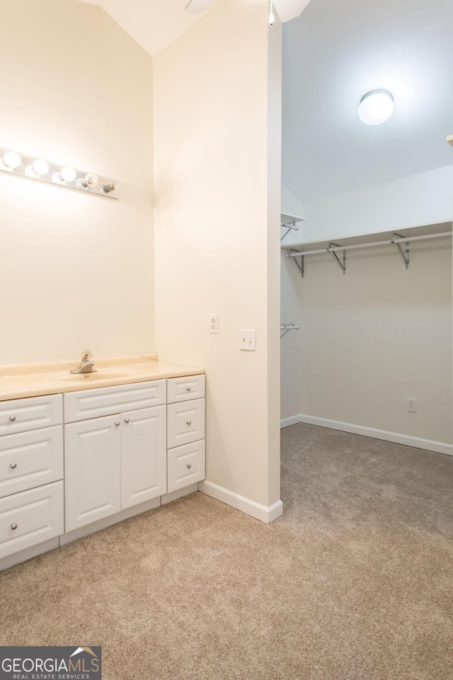 bathroom with a walk in closet, baseboards, carpet, lofted ceiling, and vanity