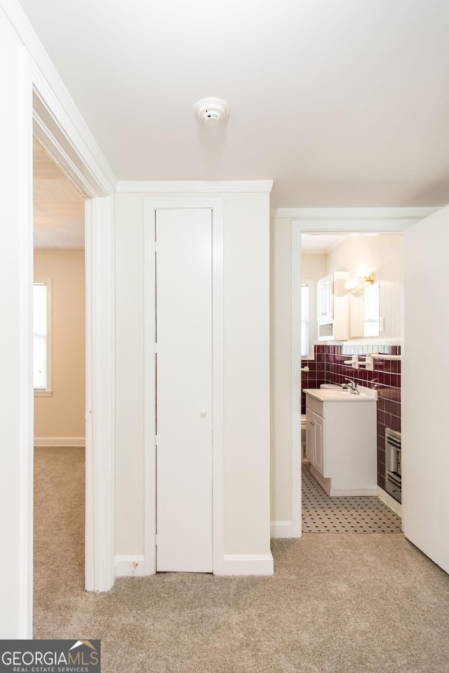 hallway with light colored carpet, tile walls, and a sink