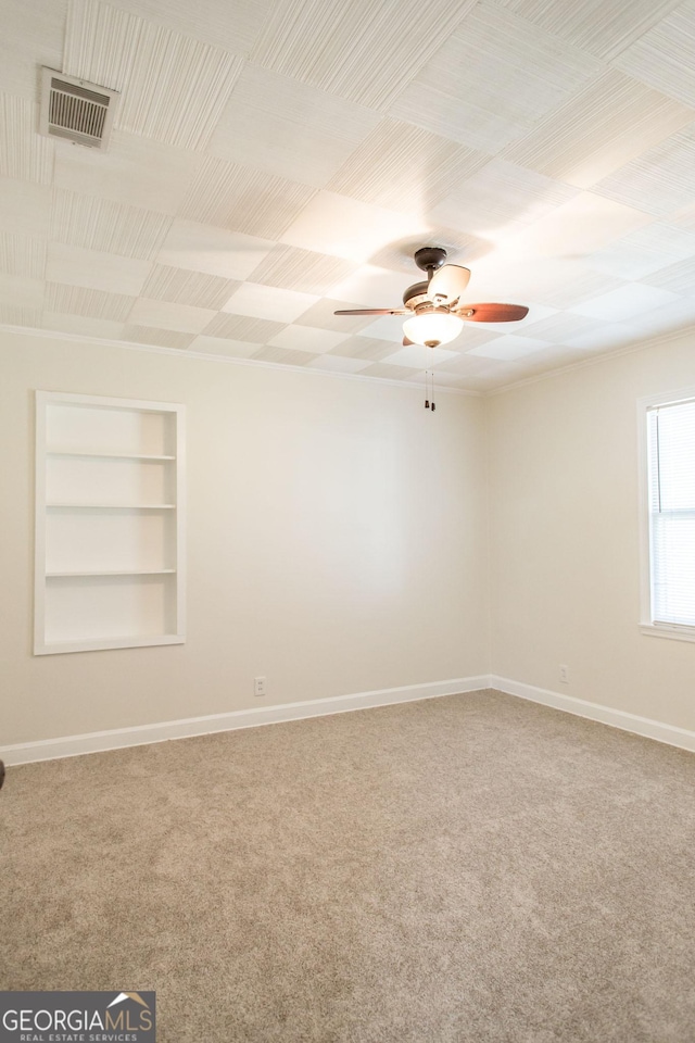 carpeted spare room featuring baseboards, built in shelves, visible vents, and a ceiling fan