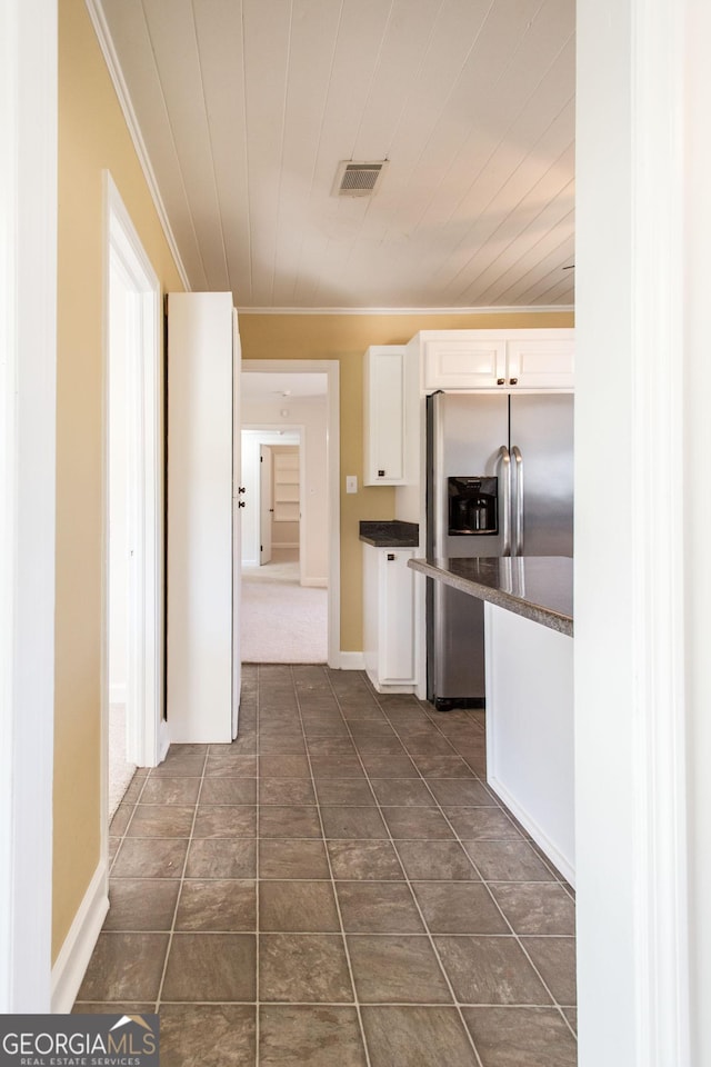 kitchen with dark countertops, visible vents, crown molding, stainless steel fridge with ice dispenser, and white cabinets