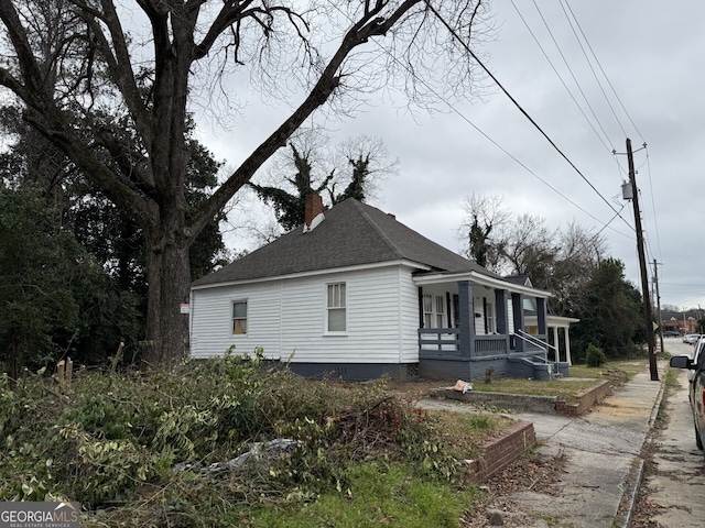 view of front of home with covered porch, a chimney, and a shingled roof