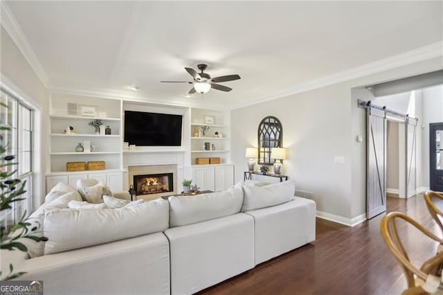 living area with baseboards, dark wood finished floors, ceiling fan, crown molding, and a barn door