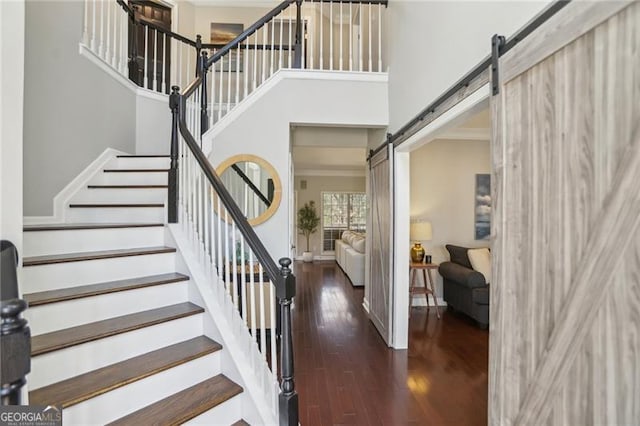 stairway featuring a barn door, wood finished floors, and a towering ceiling