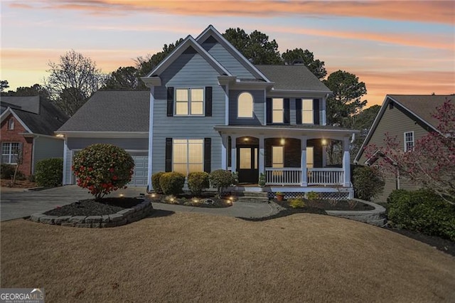 traditional home featuring an attached garage, a porch, concrete driveway, and a yard