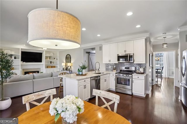 kitchen featuring light countertops, ornamental molding, a peninsula, stainless steel appliances, and a sink