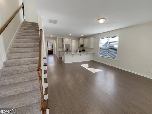 unfurnished living room featuring baseboards, visible vents, dark wood finished floors, recessed lighting, and stairs