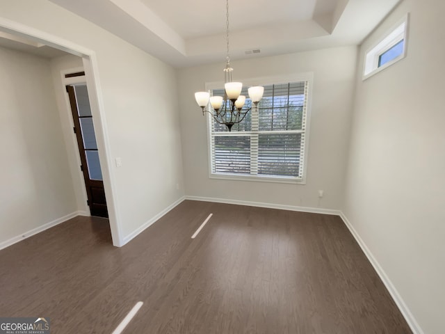 unfurnished dining area featuring visible vents, dark wood-type flooring, baseboards, a tray ceiling, and an inviting chandelier