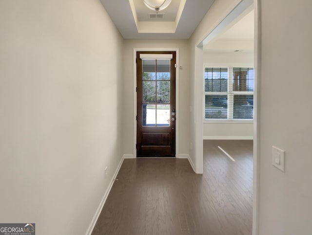 doorway with dark wood finished floors, visible vents, a raised ceiling, and baseboards