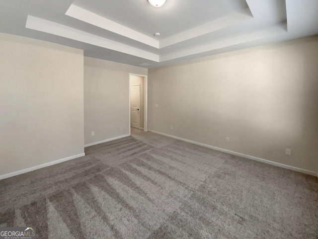 carpeted empty room featuring a tray ceiling and baseboards