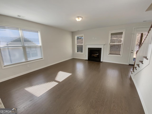 unfurnished living room with visible vents, a healthy amount of sunlight, dark wood finished floors, and stairs