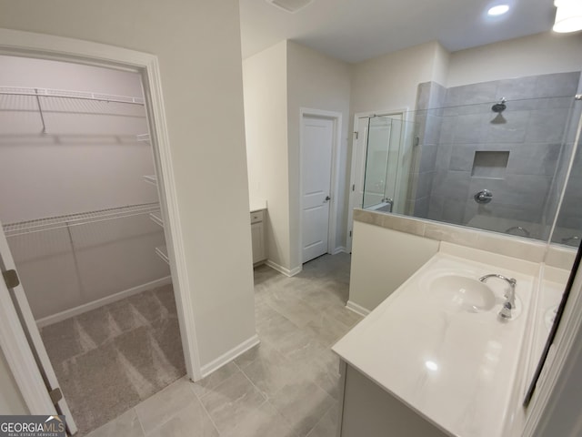 bathroom featuring baseboards, tiled shower, a spacious closet, and vanity