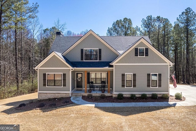 craftsman-style home featuring covered porch, a chimney, and a shingled roof