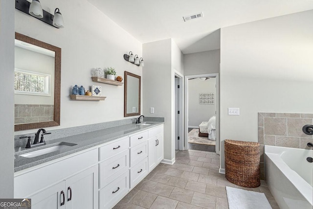 ensuite bathroom featuring a garden tub, double vanity, visible vents, and a sink