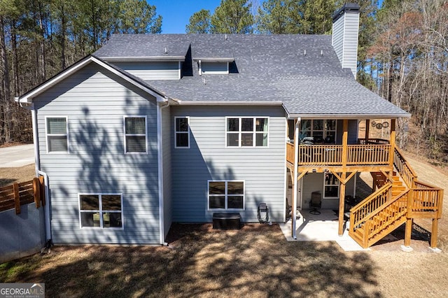 rear view of house with a patio, roof with shingles, a wooden deck, a chimney, and stairs