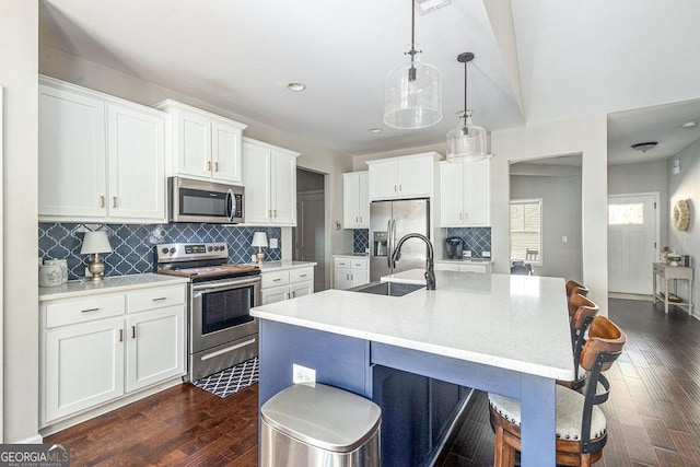 kitchen with a sink, a breakfast bar, dark wood-style floors, stainless steel appliances, and a kitchen island with sink