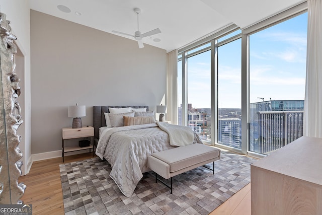 bedroom featuring access to exterior, baseboards, expansive windows, light wood-style flooring, and a ceiling fan