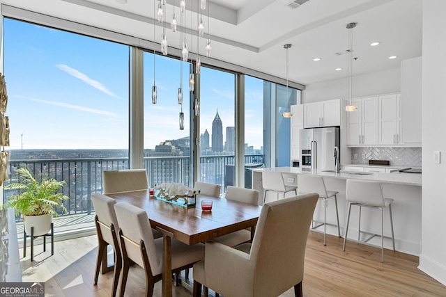 dining area featuring a wealth of natural light, a city view, a wall of windows, and light wood-type flooring