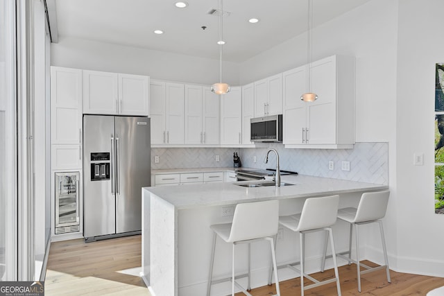 kitchen with a peninsula, a sink, wine cooler, appliances with stainless steel finishes, and backsplash