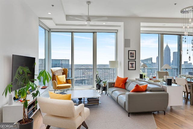 living room with expansive windows, a city view, wood finished floors, and ceiling fan with notable chandelier