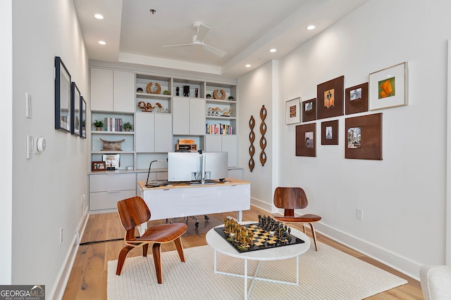 home office featuring light wood-style flooring, a ceiling fan, a tray ceiling, recessed lighting, and baseboards