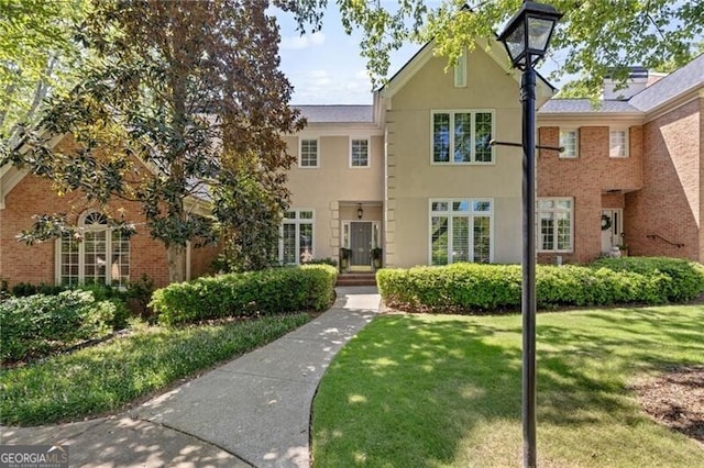 view of front of property featuring brick siding, stucco siding, and a front yard