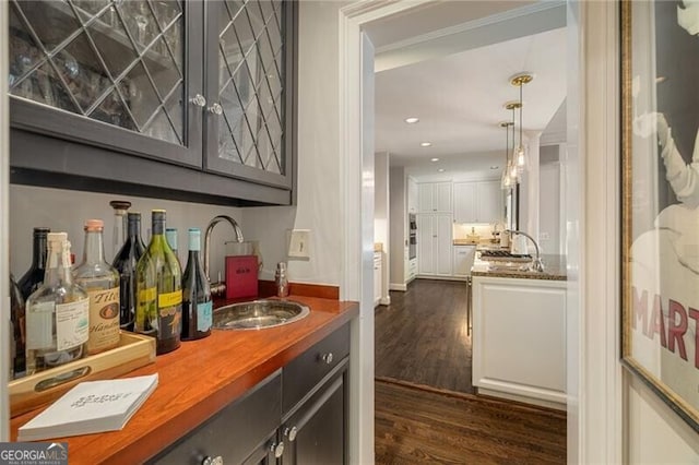 bar featuring dark wood-type flooring, recessed lighting, wet bar, hanging light fixtures, and a sink