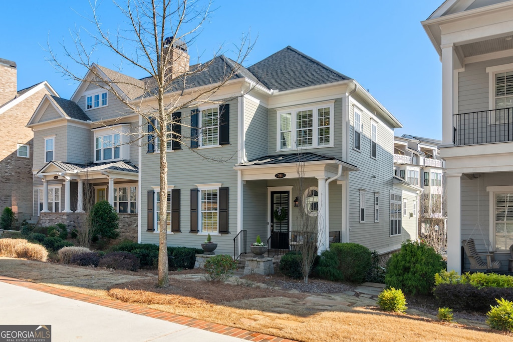view of front facade with roof with shingles, a standing seam roof, covered porch, a chimney, and metal roof