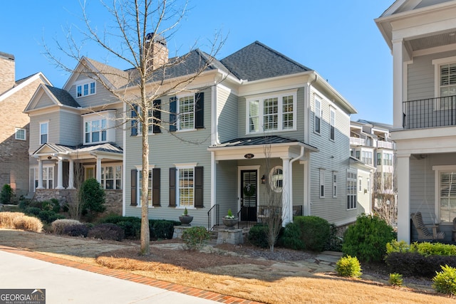 view of front facade with roof with shingles, a standing seam roof, covered porch, a chimney, and metal roof