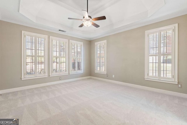 carpeted spare room with visible vents, crown molding, baseboards, a raised ceiling, and a ceiling fan