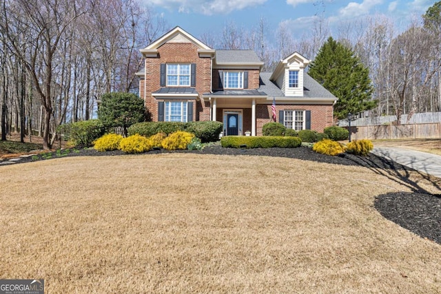 traditional home with a front yard, fence, and brick siding