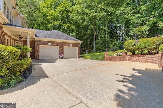 view of side of home featuring brick siding, concrete driveway, a garage, a ceiling fan, and roof with shingles
