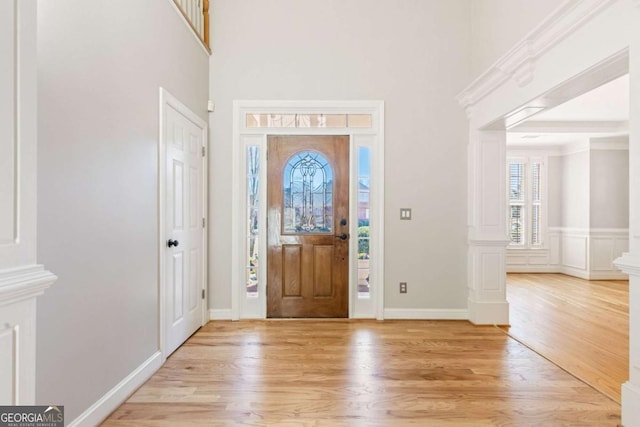 entryway with light wood-style flooring, ornate columns, and a towering ceiling