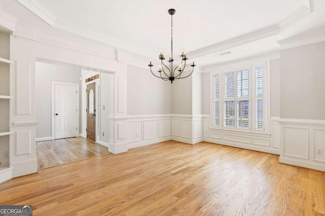 unfurnished dining area featuring a chandelier, crown molding, wood finished floors, a tray ceiling, and a wainscoted wall