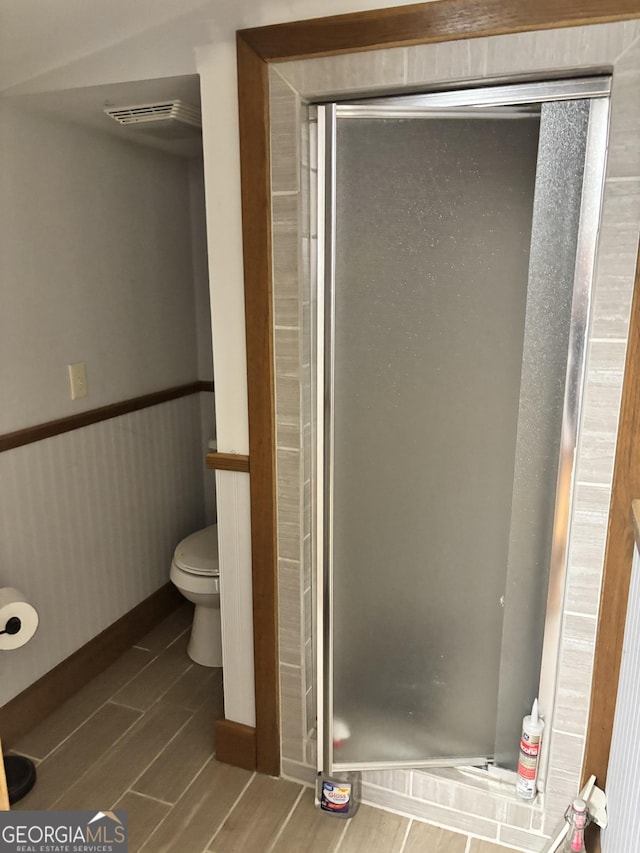 full bathroom featuring a wainscoted wall, visible vents, toilet, a stall shower, and wood finished floors