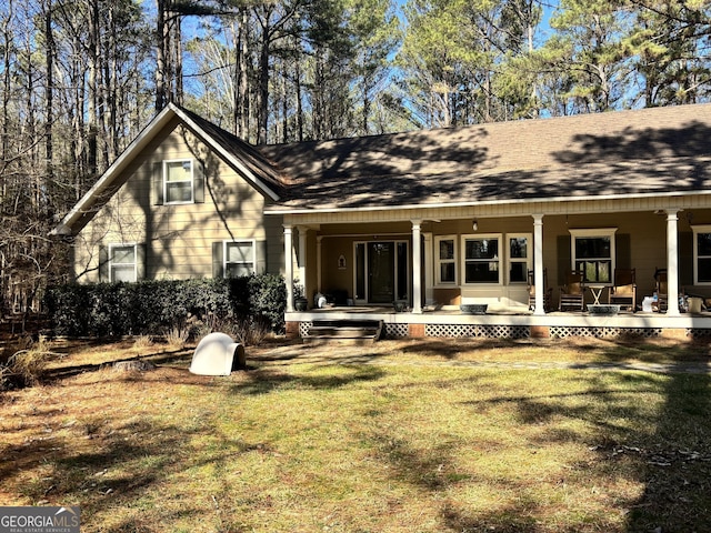 rear view of house featuring a yard, roof with shingles, and covered porch