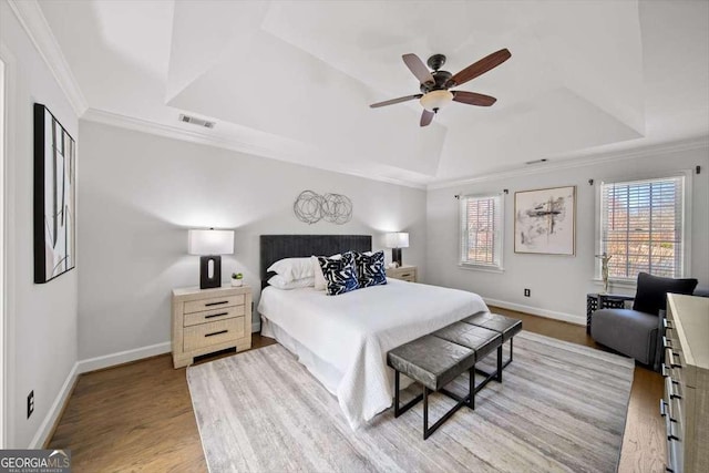 bedroom with visible vents, light wood-style flooring, ornamental molding, a tray ceiling, and baseboards