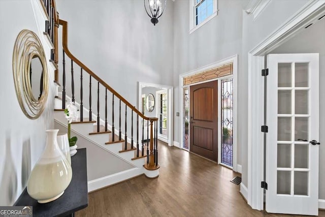 foyer featuring visible vents, baseboards, stairway, a towering ceiling, and wood finished floors