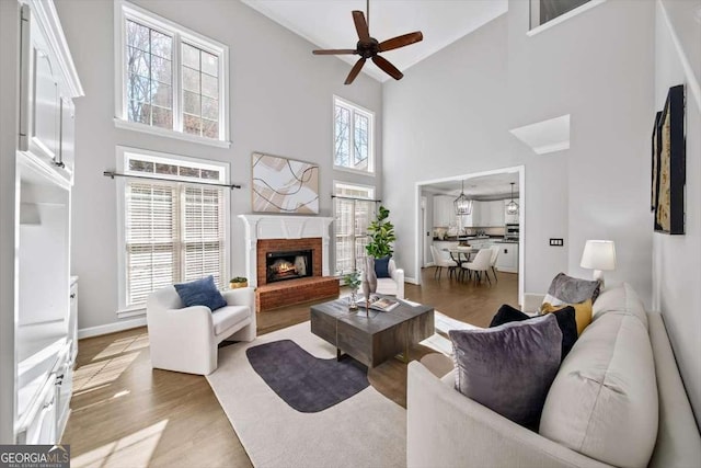 living area with a fireplace, wood finished floors, baseboards, and a ceiling fan