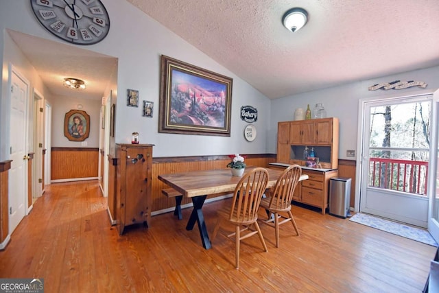 dining room featuring a wainscoted wall, light wood finished floors, a textured ceiling, and vaulted ceiling