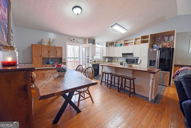 dining area featuring a textured ceiling, light wood-style flooring, and vaulted ceiling