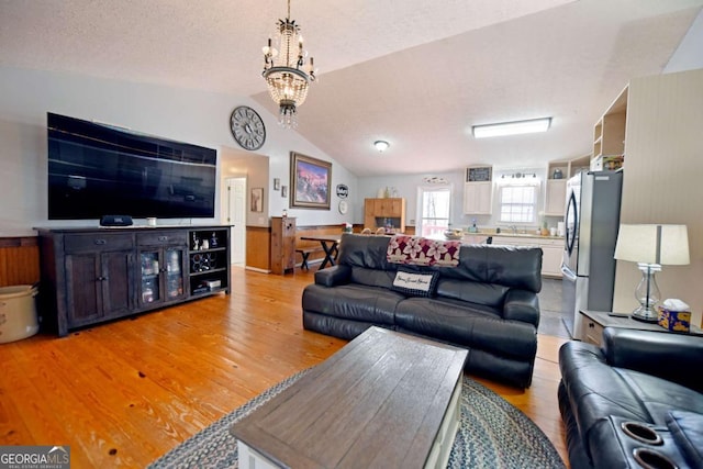 living room with an inviting chandelier, vaulted ceiling, light wood-type flooring, and a textured ceiling