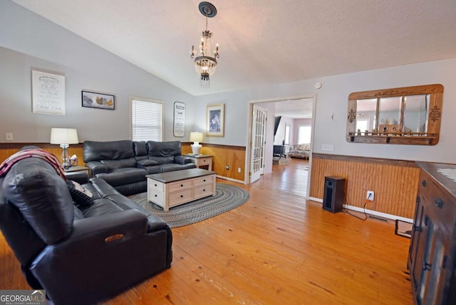 living room featuring a wainscoted wall, wood-type flooring, wooden walls, a chandelier, and vaulted ceiling