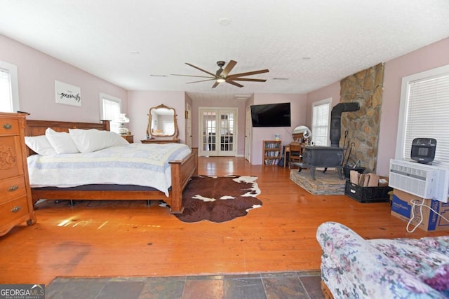 bedroom featuring wood finished floors, a wood stove, ceiling fan, an AC wall unit, and french doors