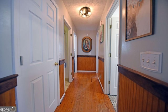 corridor featuring a wainscoted wall, a textured ceiling, and light wood-style floors