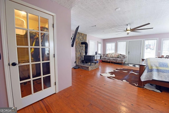 living area with a healthy amount of sunlight, a textured ceiling, a wood stove, and wood-type flooring